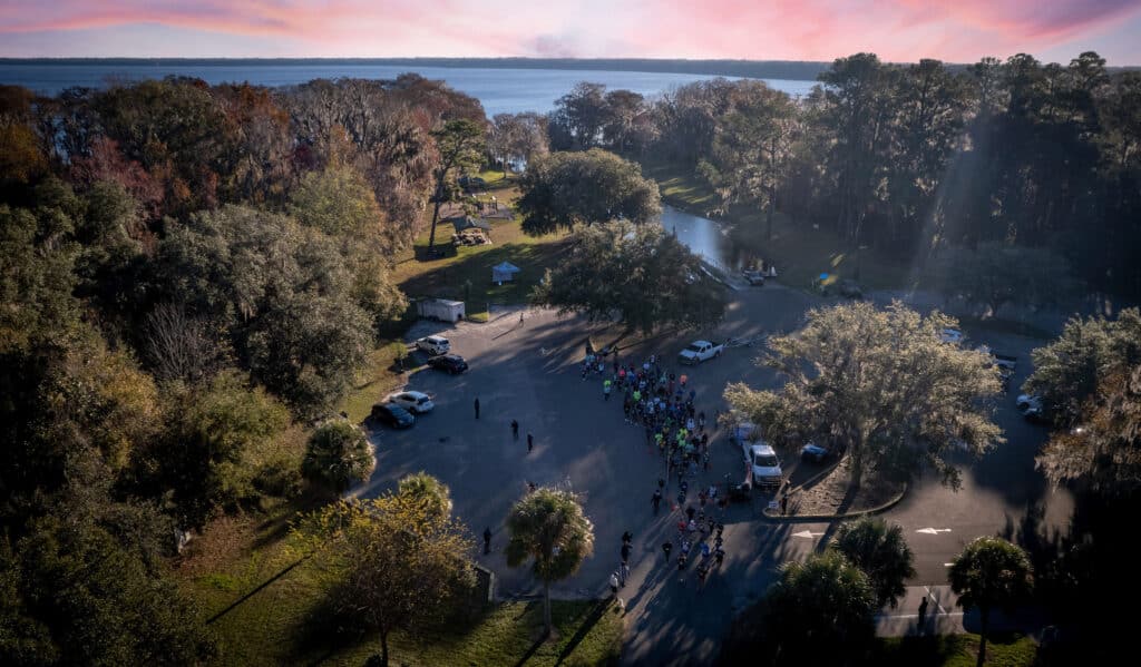 An aerial view of the Gainesville running club gathered in a parking lot near a lake at sunrise.