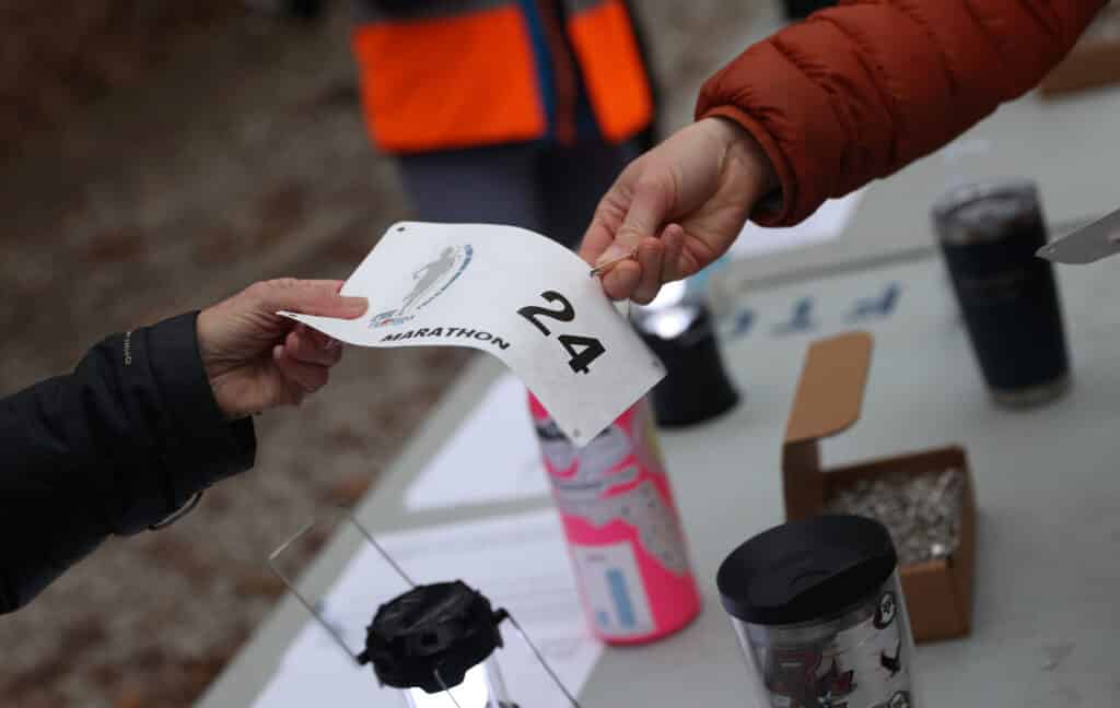 A person hands a race bib numbered 24 to another member of the Gainesville Running Club.