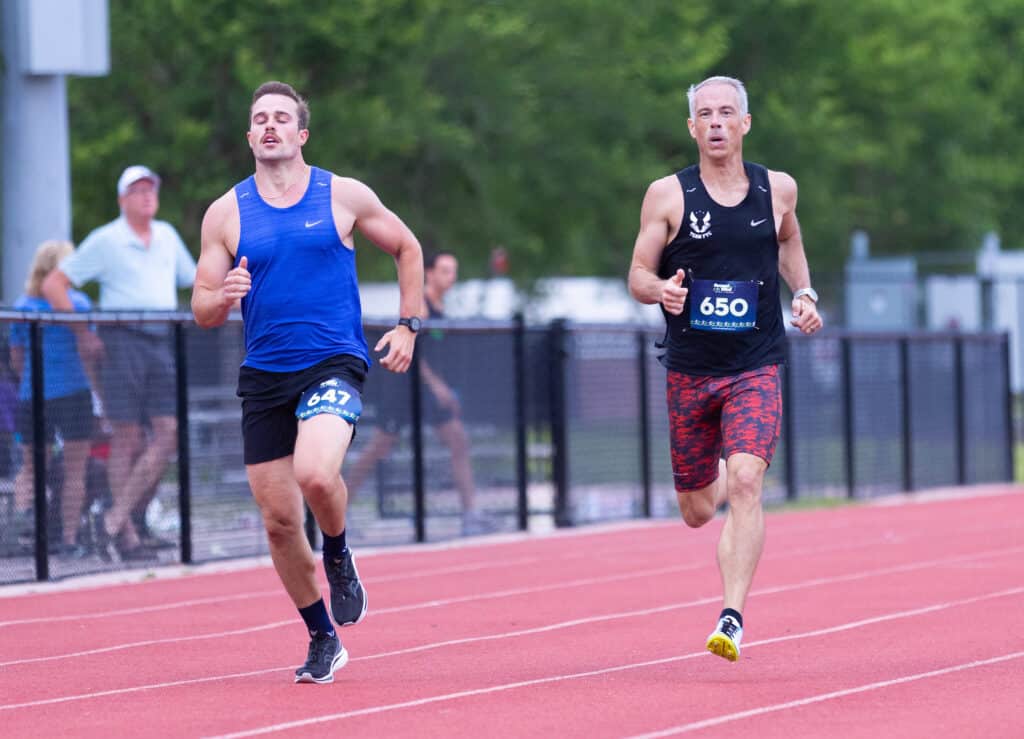 Two male runners with bib numbers 647 and 650 compete on a track for the Florida Track Club.