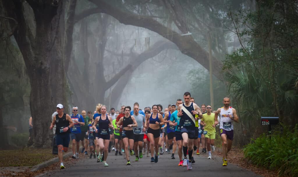 Members of the Gainesville Run Club participate in a road race on a foggy path lined with moss-covered trees.