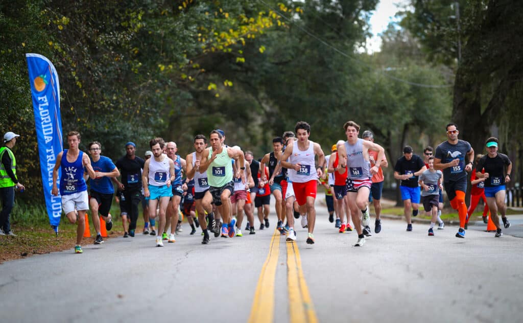 A large group from the Florida Track Club participating in a road race on a paved street.