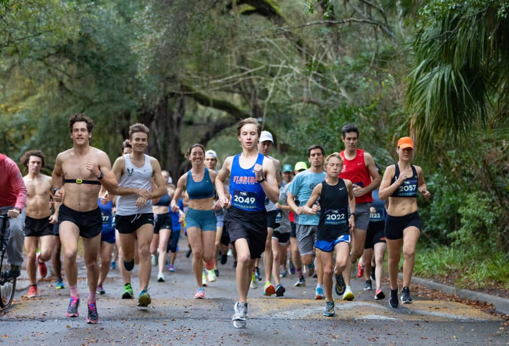 A large group of Gainesville Run Club members participating in a road race on a wooded path.