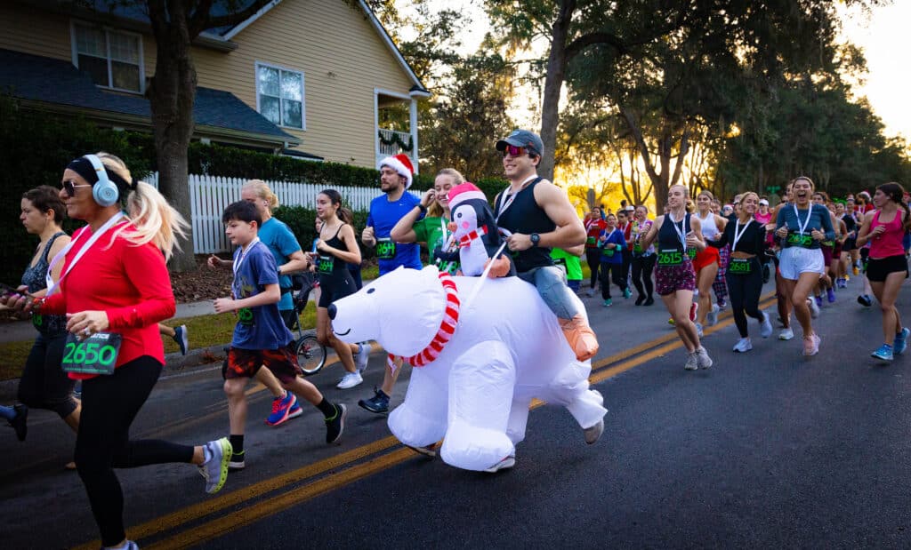 A runner in an inflatable polar bear costume runs alongside a large group from the Gainesville Running Club participating in a road race.