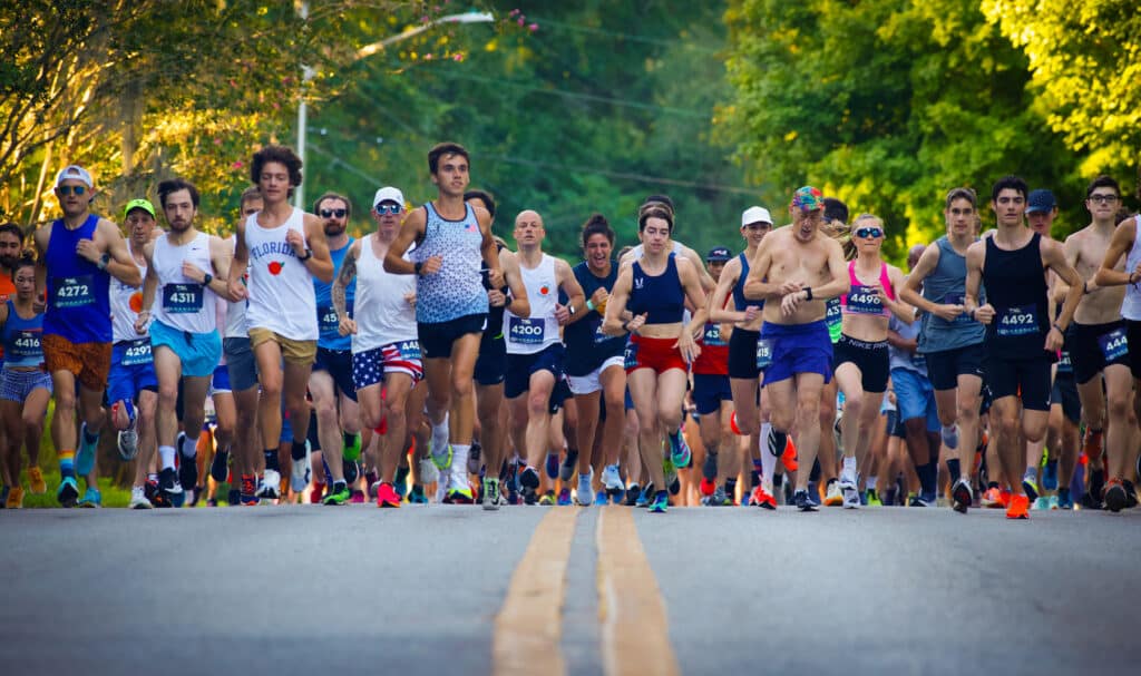 A large group from the Florida Track Club wearing race bibs and athletic gear run together down a paved road.