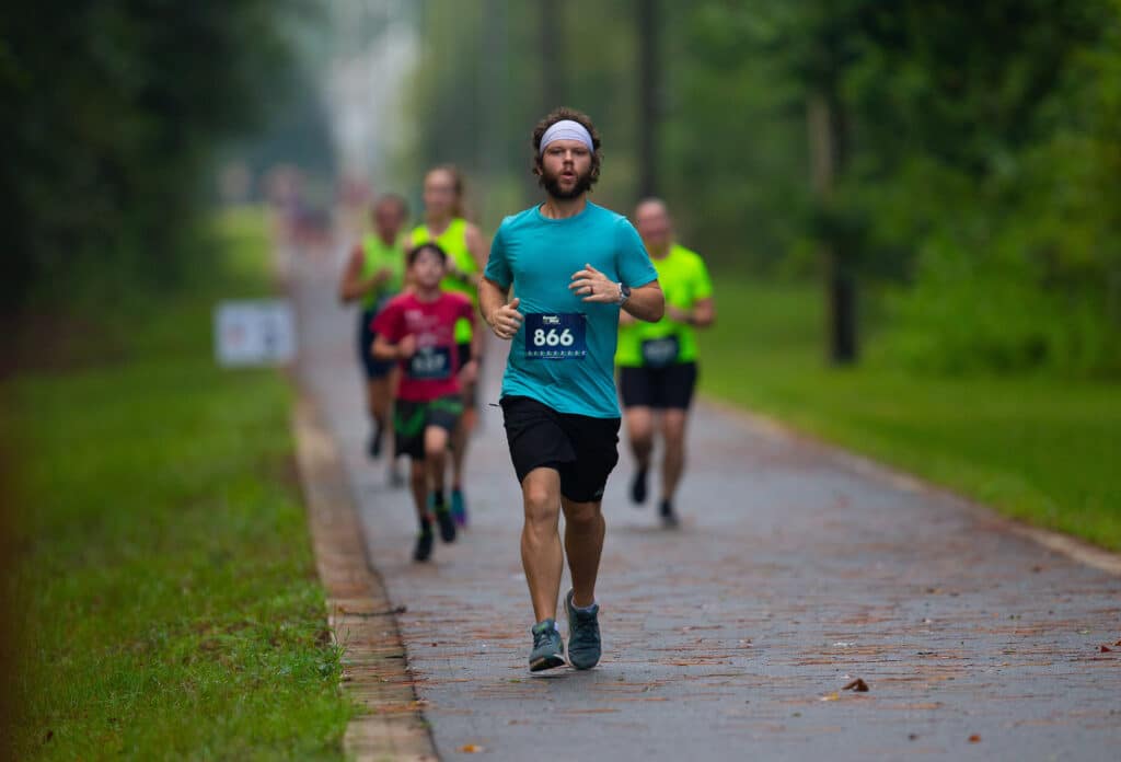 A runner with a headband and race bib number 866 leads the Gainesville Run Club along a paved path.