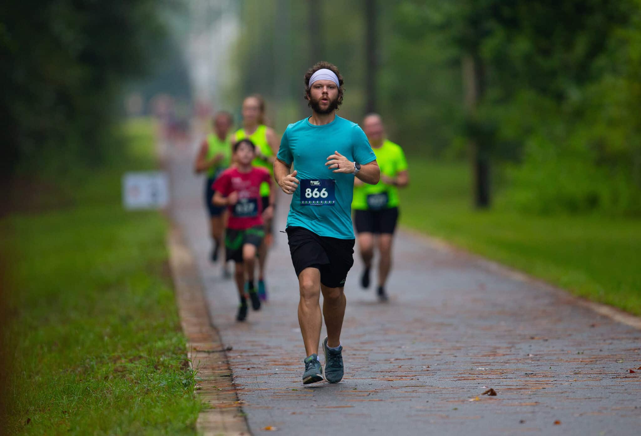 A runner with a headband and race bib number 866 leads the Gainesville Run Club along a paved path.