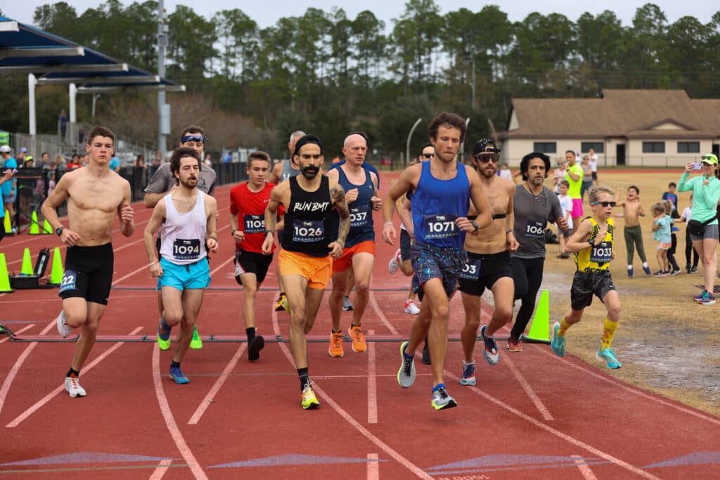 A group of male runners from the Gainesville running club wearing race bibs while competing in a track race.