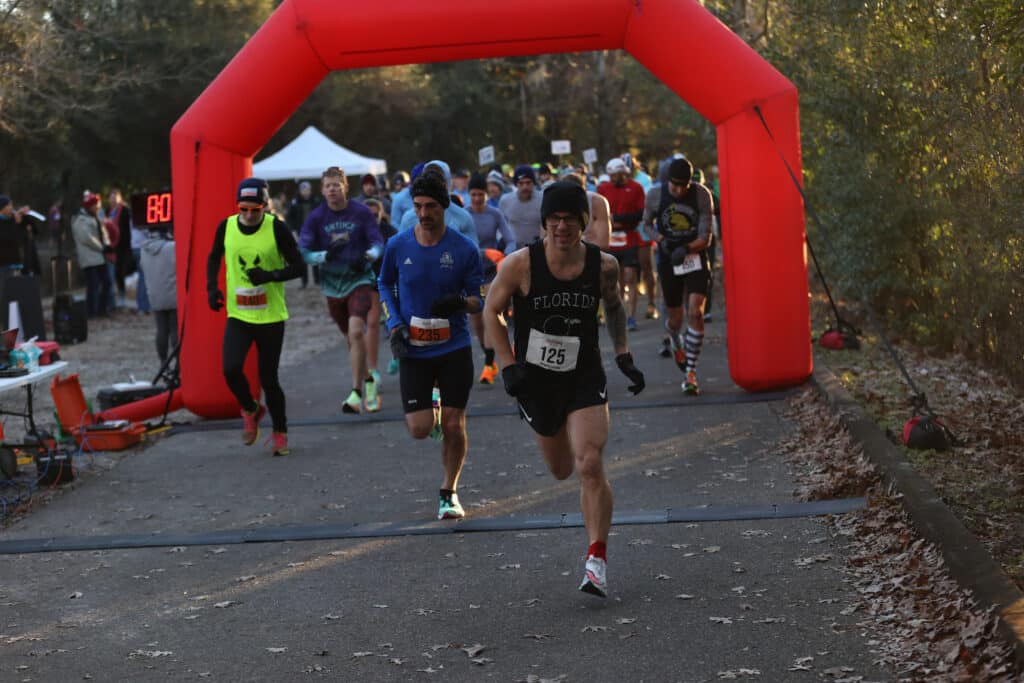 A group of Florida Track Club runners approach a large red inflatable arch at the finish line of a race.