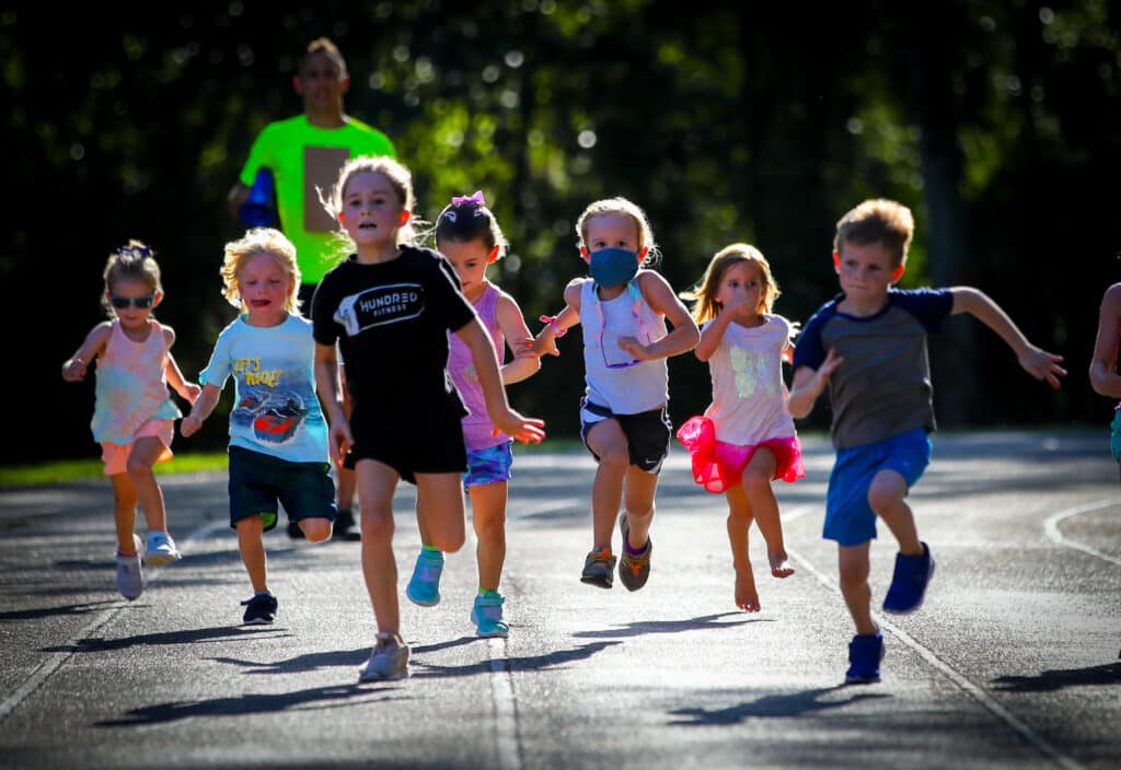 A group of young children from the Gainesville Run Club running together on a track during an outdoor fitness event.