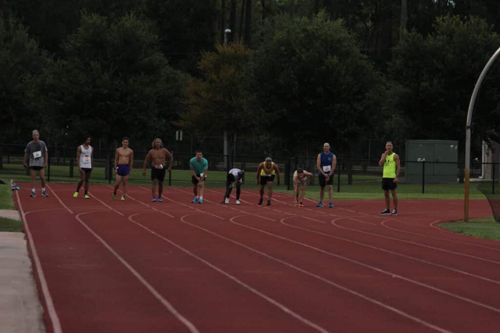 Members of the Gainesville Running Club stand on a red track, some in starting positions and others standing at the sports field.