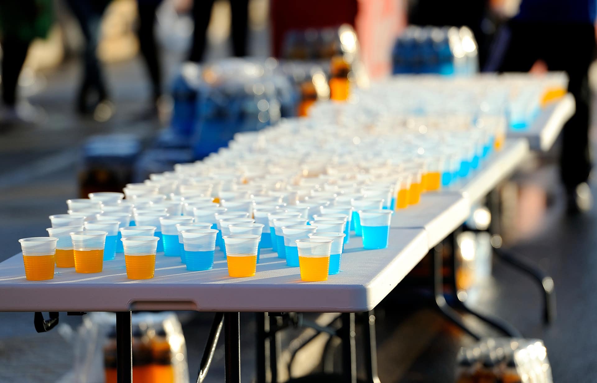 A long table at a Gainesville running club event is covered in rows of small plastic cups filled with orange and blue liquid.