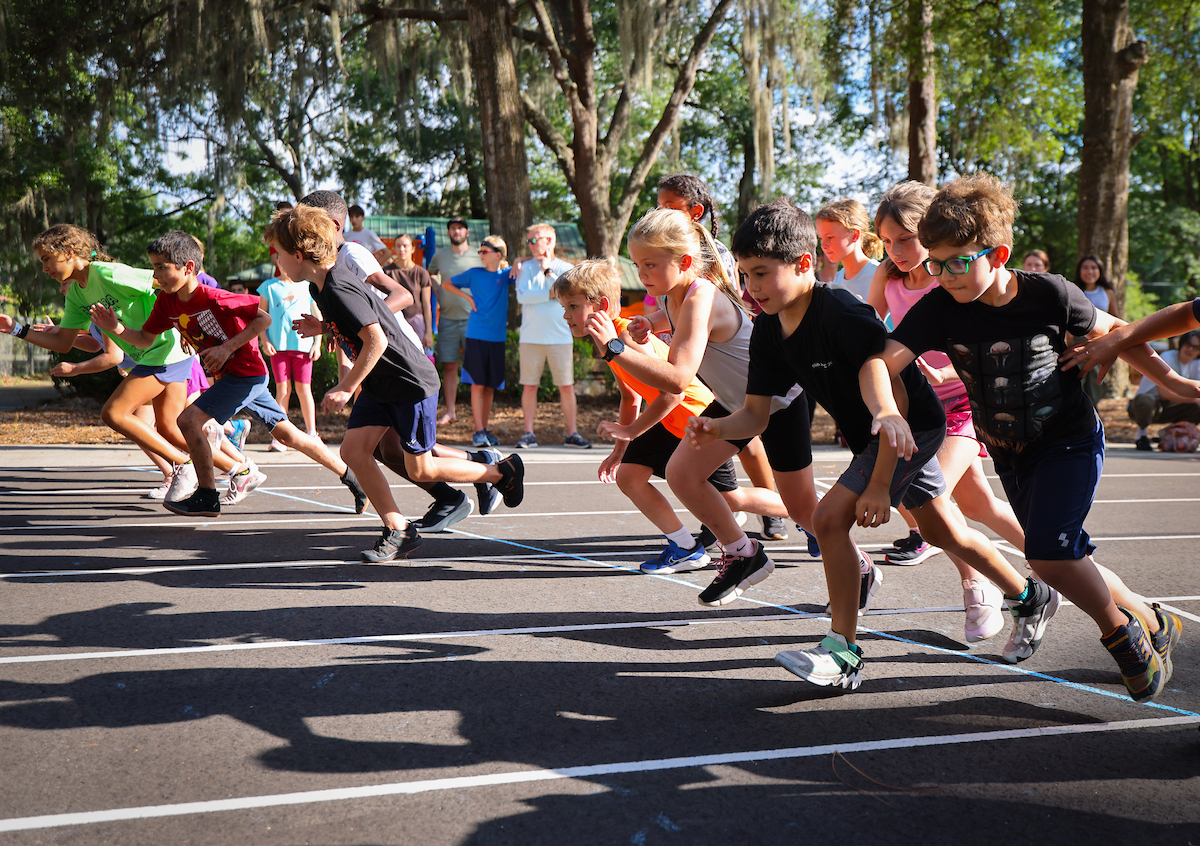 A group of children from the Gainesville run club crouch at the starting line of a track, ready to run.